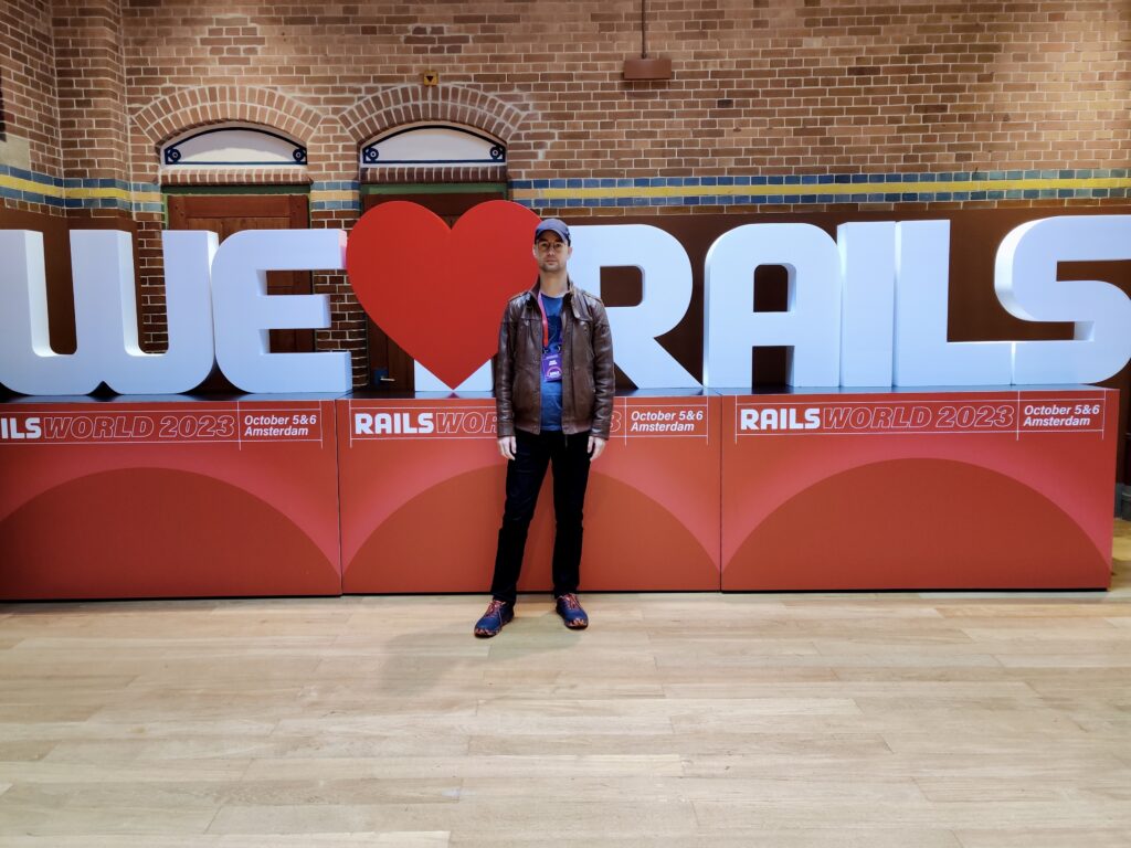 Ivan at Rails World, the Ruby on Rails annual conference, standing in front of the We Love Rails logo.